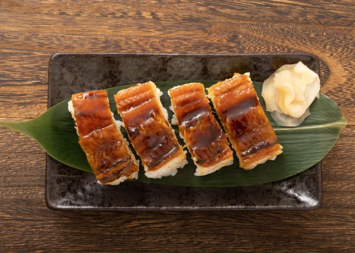 Anago nigiri sushi served on a leaf, shiny with sauce.